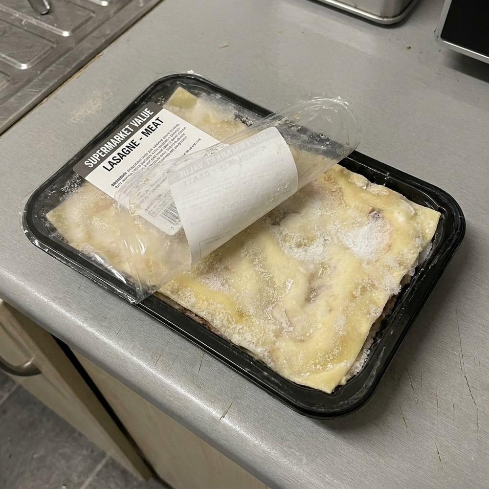 A frozen ready meal in a black plastic tray with the film half peeled back